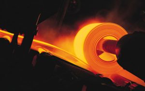 a large hot orange steel sheet is being rolled by a machine in a steel mill